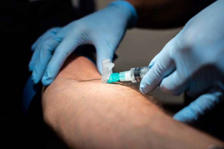 A close-up of a syringe being inserted into a male white patient's arm